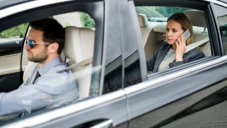 Businesswoman sitting on back seat in taxi car, talking on the phone.